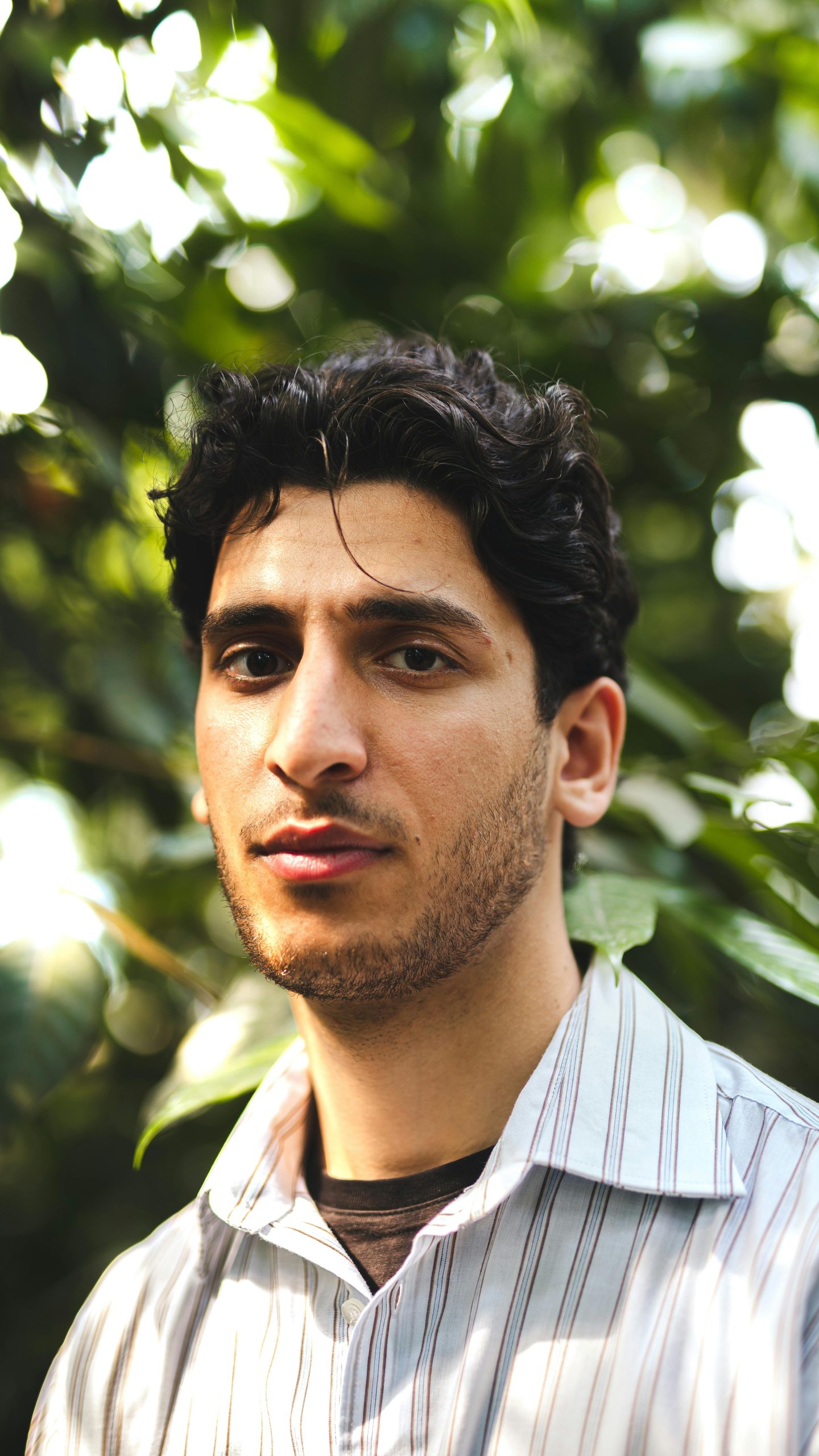 Portrait of a young man in an outdoor setting with natural light, exuding a casual yet thoughtful expression.