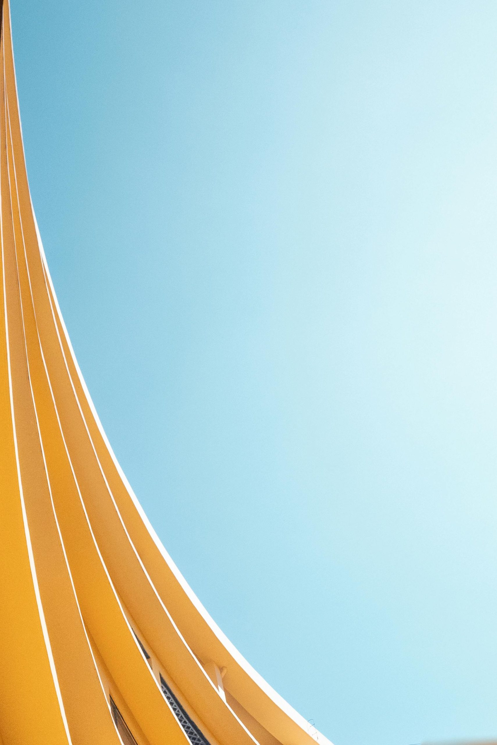 Abstract view of a modern yellow curved structure against a clear blue sky.